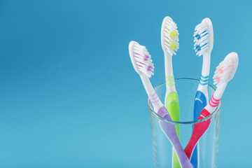 Toothbrushes of different colors in a transparent glass on a blue background.
