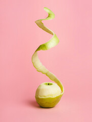 Half peeled fresh green apple with flying peel on pastel pink background. Creative fruit concept...