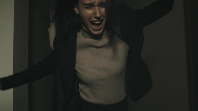 Tracking shot of young woman screaming and running away from zombie in hallway