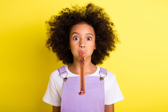 Portrait of pretty funky childish wavy-haired girl blowing whistle accessory isolated over bright yellow color background