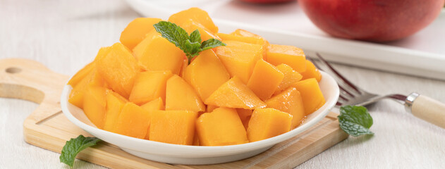 Diced fresh mango fruit on a white plate with leaves.