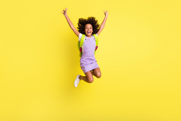 Full length body size photo of funny schoolgirl jumping high with rucksack laughing careless isolated vivid yellow color background