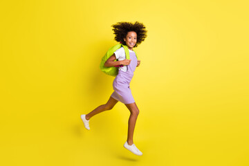 Fototapeta na wymiar Full length body size view of cheerful wavy-haired girl jumping running back to school lesson isolated over bright yellow color background