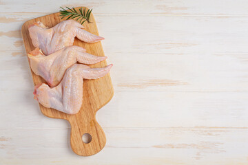 Raw chicken wings on the white wooden background.