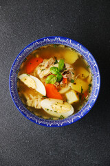 Chicken noodle soup with egg, vegetables and chicken meat on dark backdrop top view