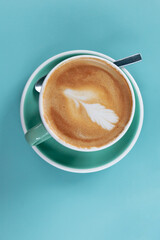 A hot latte in a green ceramic cup on a  blue turquoise background with copy space
