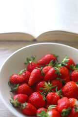 Bowl of strawberries and open book on a table. Selective focus.