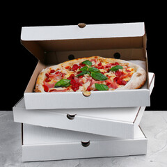 meat pizza inside box. stack of pizza boxes standing on concrete table and black background