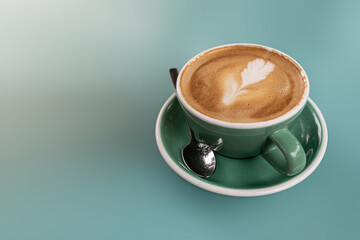 A hot latte in a green ceramic cup on a  blue turquoise background with copy space