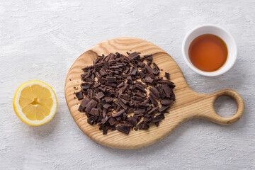 Wooden board with chopped bitter chocolate, Jerusalem artichoke syrup and half lemon on light gray textured background