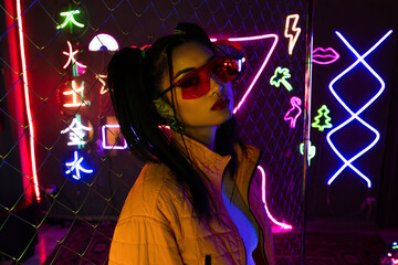 young asian woman in sunglasses looking at camera near neon sign