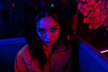 stylish young asian woman looking at camera near neon lighting