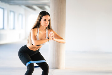 Fototapeta na wymiar Attractive young woman exercising squats with resistance band. Photo of caucasian girl wearing fitness clothes.