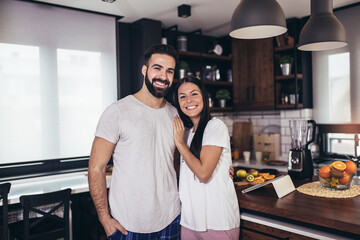 Happy young couple posing in modern kitchen while preparing breakfast.