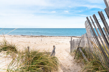 Path lined with a weathered fence through sand dunes to a beautiful deserted sandy beach on a...