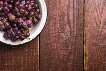 Fresh ripe grape berries in bowl on brown wooden background, top view copy space