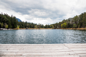 Wooden platform on a beautiful small mountain lake surrounded by pine trees in the European Alps on stormy spring day