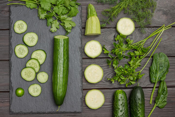 Sliced cucumber, cilantro on cutting board. Sliced zucchini, spinach and parsley on table