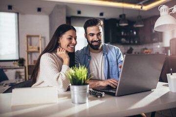 Cheerful loving young couple using laptop and analyzing their finances
