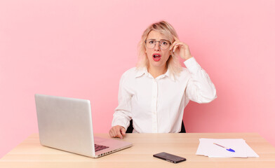 blonde pretty woman young pretty woman looking happy, astonished and surprised. workspace desk...
