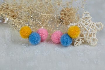 Obraz na płótnie Canvas Colored pompon earrings in the shape of three furry balls.Earrings are next to rattan products, flower specimens and other ornaments