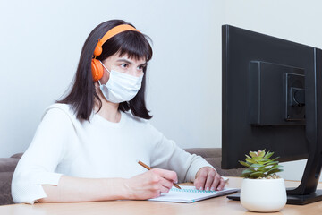 Fototapeta na wymiar A woman doctor in a medical mask and headphones makes an online video call with a patient, signs a document