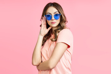 Trendy young woman in blue sunglasses posing over pink background
