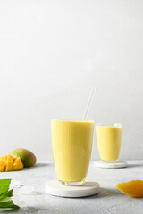 Indian ayurvedic mango lassie or lassi on light gray background. Vertical format. Mango lassie traditional healthy beverage with yogurt, water, spices, fruits and ice.