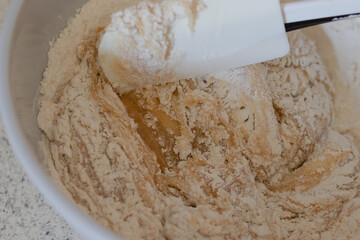 Brown sugar, white granulated sugar, melted butter, and flour, baking soda and powder being combined to make a homemade chocolate chip cookie dough recipe.