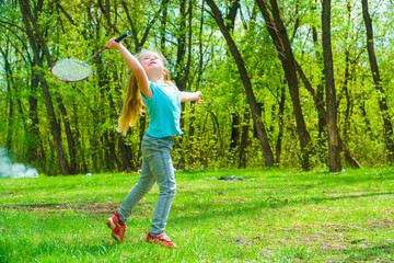 A cute girl plays badminton on a green meadow.