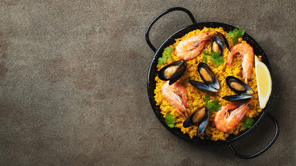 Traditional spanish seafood paella in pan with chickpeas, shrimps, mussels, squid on brown concrete background. Top view with copy space. Banner