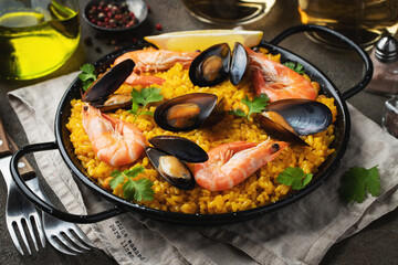 Traditional spanish seafood paella in pan with chickpeas, shrimps, mussels, squid on brown concrete background.