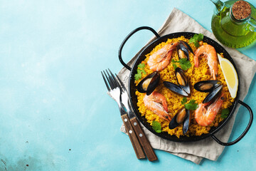 Traditional spanish seafood paella in pan with chickpeas, shrimps, mussels, squid on light blue concrete background. Top view with copy space