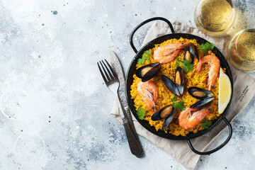 Traditional spanish seafood paella in pan with chickpeas, shrimps, mussels, squid on light grey concrete background. Top view with copy space
