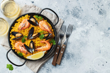 Traditional spanish seafood paella in pan with chickpeas, shrimps, mussels, squid on light grey concrete background. Top view with copy space