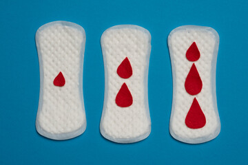 Three woman's sanitary pads with artificial red drops, isolated on blue background.