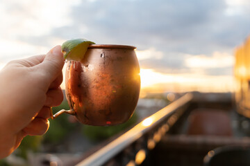 A moscow mule held up at a rooftop restaurant bar at sunset