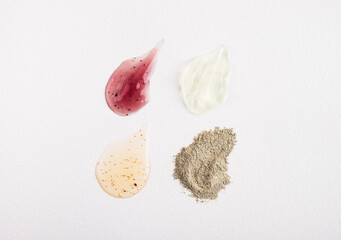Cosmetic products smears on white background. Beauty, facial and body skincare: serum essence, moisturizer, natural scrub and green clay. Top view