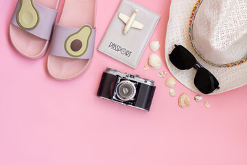 Female white hat, passport, black sunglasses, old vintage retro camera, flip-flops with avocado halves, toy plane, seashells isolated on a light color pink background. Summer vacation travel concept