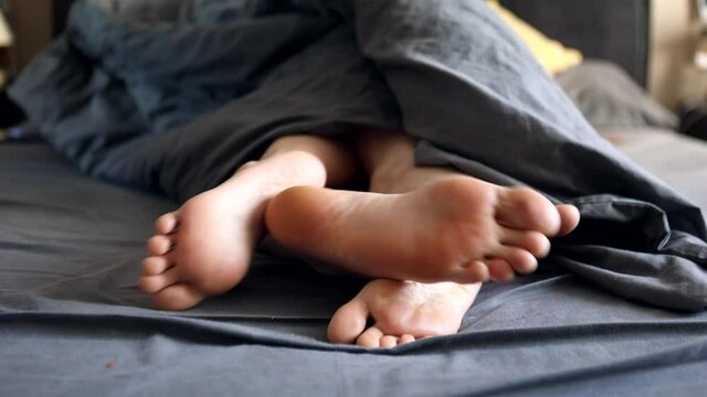 couple legs woman and man under the grey blanket in bed