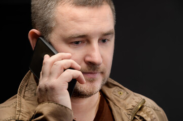 Close-up portrait of a caucasian businessman in a casual jacket talking on the phone upset looking to the side and down. A distressed man is sad with a phone in his hand. Studio shot