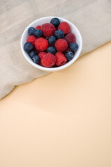 detail of raspberries and blueberries in a bowl on a beige table