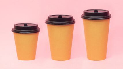 Three brown craft paper cups small 0,3 l,medium 0,4 land big 0,5 l with black lids of tea or coffee isolated on a pink background. Mockup with empty copy space for text or design. Eco-friendly 