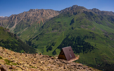 A lonely wooden house on the slope of Mount Cheget overlooking the slopes of Mount Sarykolbashi-Tersak. Elbrus region. July 2020. Landscape view in the east of mount from Cheget mount. Kabardino