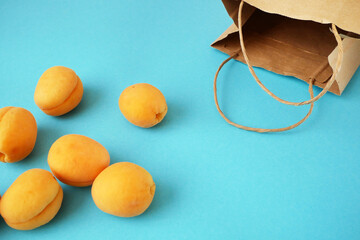 paper bag and many juice tasty ripe apricots fruits on blue background, zero waste concept, closeup