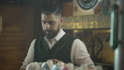 The bartender wipes a beer glass. The work of the bartender at the bar. The bartender is sad and sighs at the wiping glass. Beautiful interior of the restaurant.