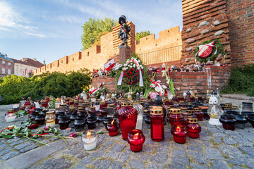 Warsaw Uprising Memorial Day, flowers, candles and Polish flags near Little Insurrectionist sculpture, a statue of the child soldiers. Honoring victims of 1944 revolt - obrazy, fototapety, plakaty