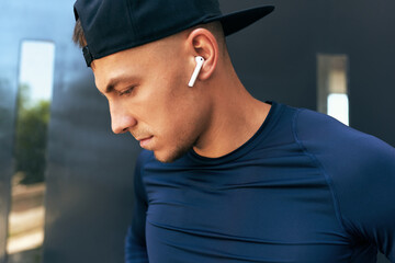 Outdoor closeup portrait of an athlete man taking a break after workout ad listening the music in earphoens in the city street.