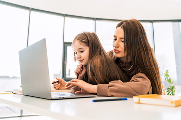 Mother and daughter are doing homework at the laptop. Little schoolgirl at the distance learning at home