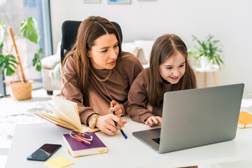 Mom and little daughter doing homework on laptop. Mother teaches the child at home